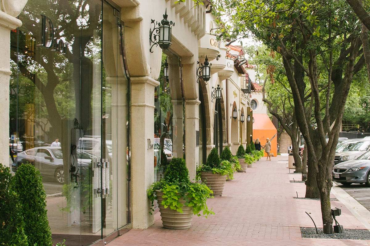 Contemporary view of the shaded sidewalks and Spanish Mediterranean storefronts at Highland Park Village