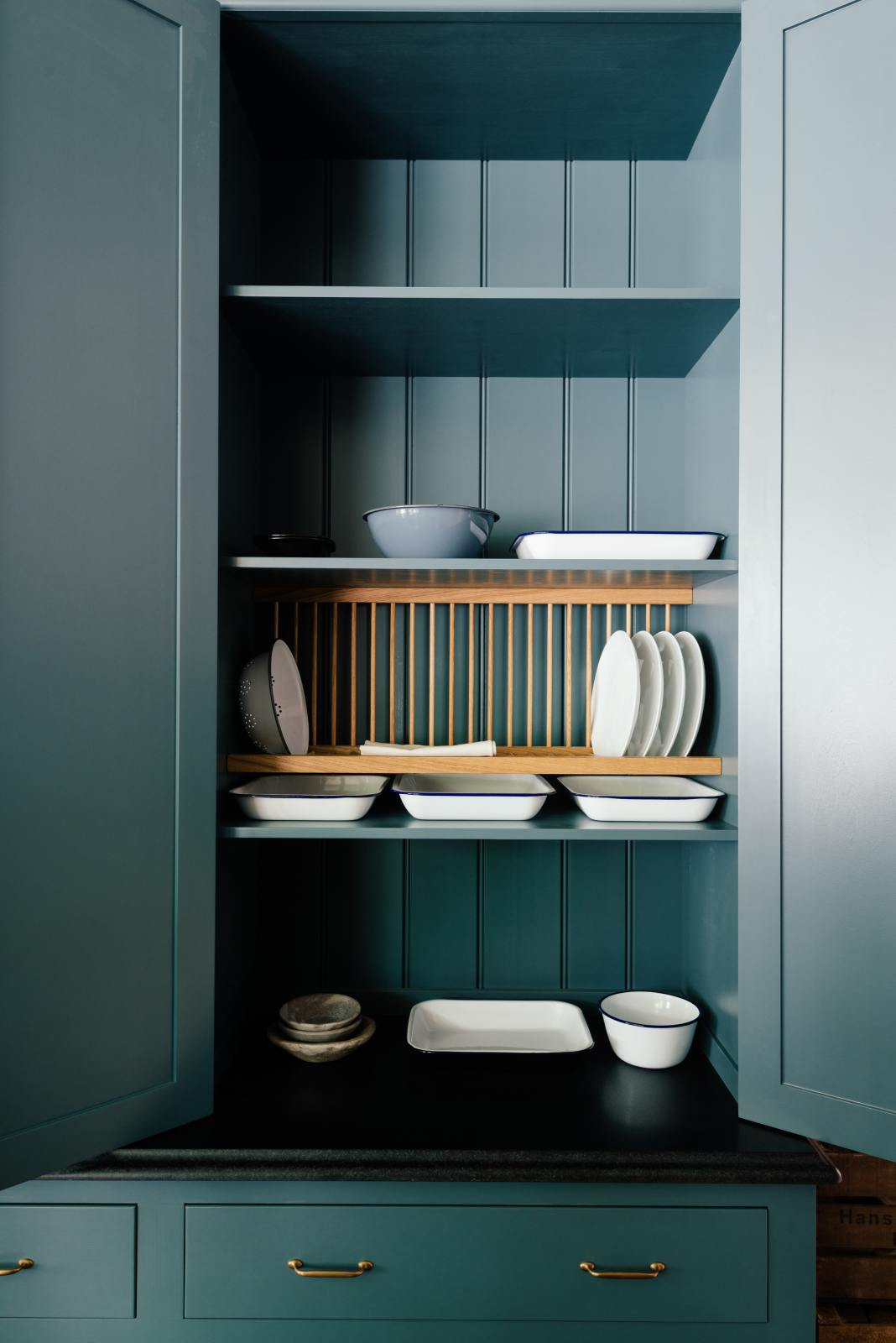 Open blue pantry with shelves of ceramics and a wooden plate rack.