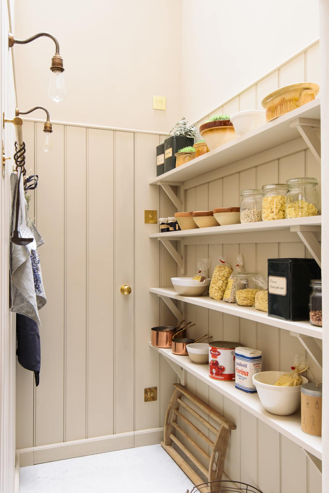 Narrow beige pantry stocked with jars, tins and copper cookware.